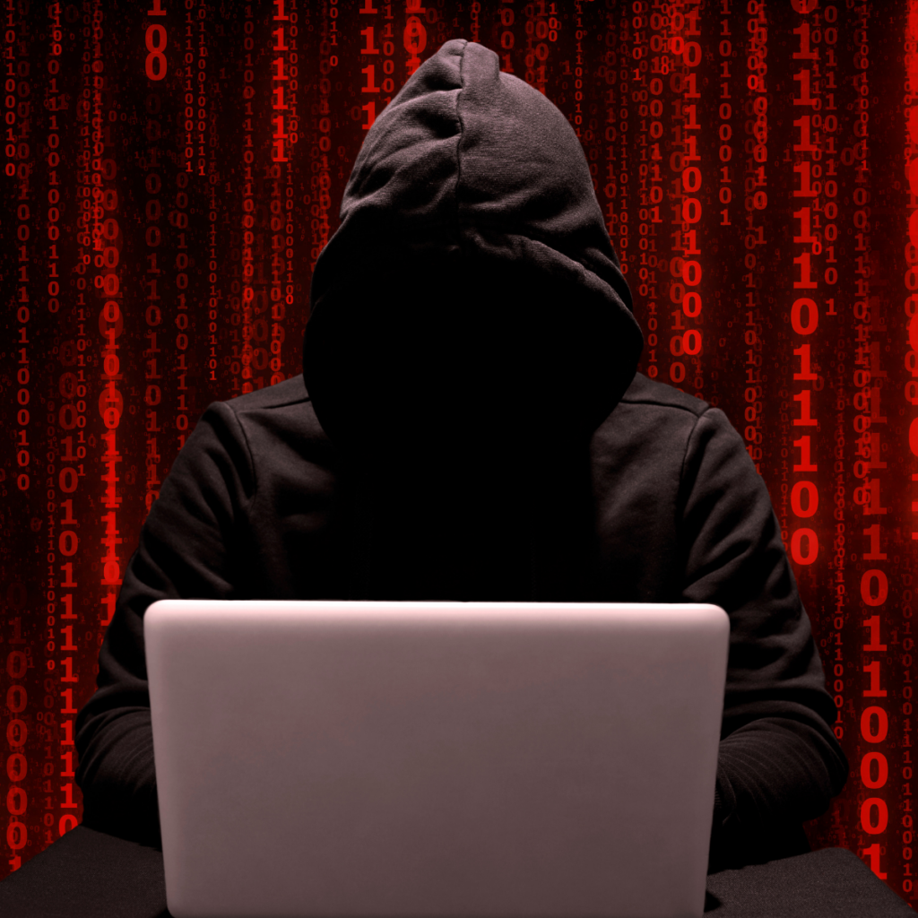 cyber criminal with hood up behind a laptop with red coding as a background