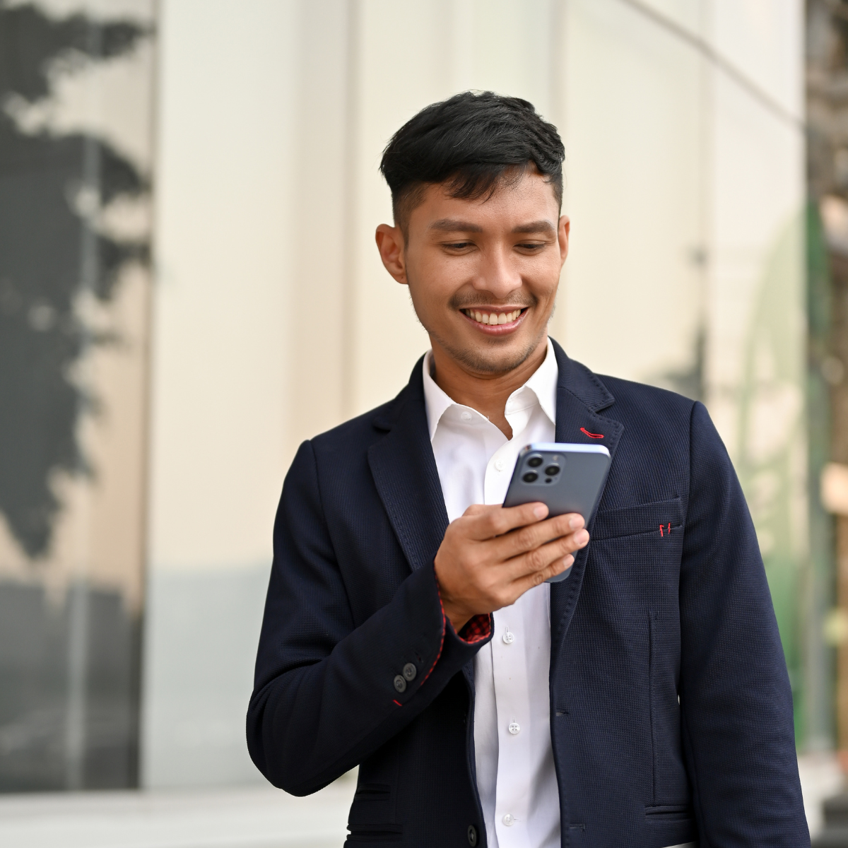 young man on phone in street, smiling at his device