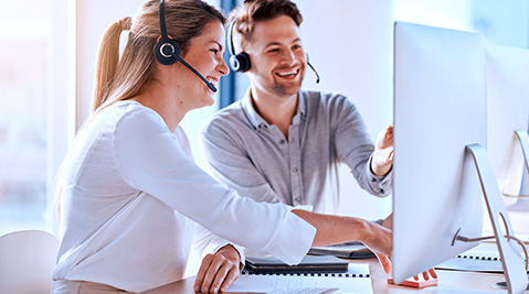 Two Work colleagues smiling at a computer screen.